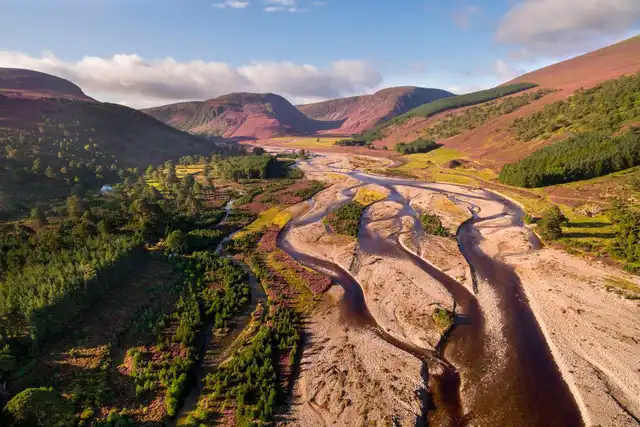 A braided river winding through a heather-covered glen in the Cairngorms