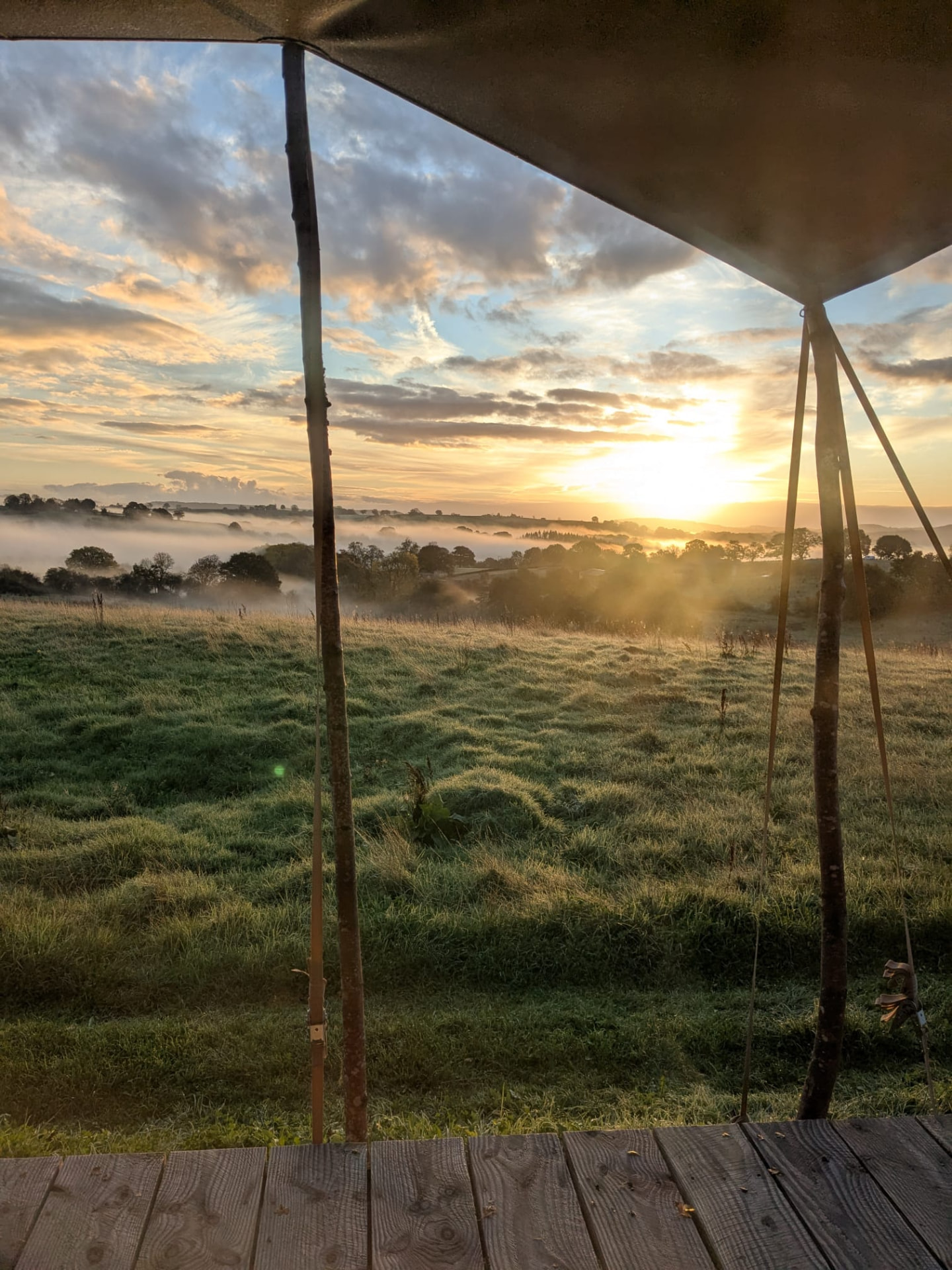 The view from a glamping tent across misty fields at sunrise